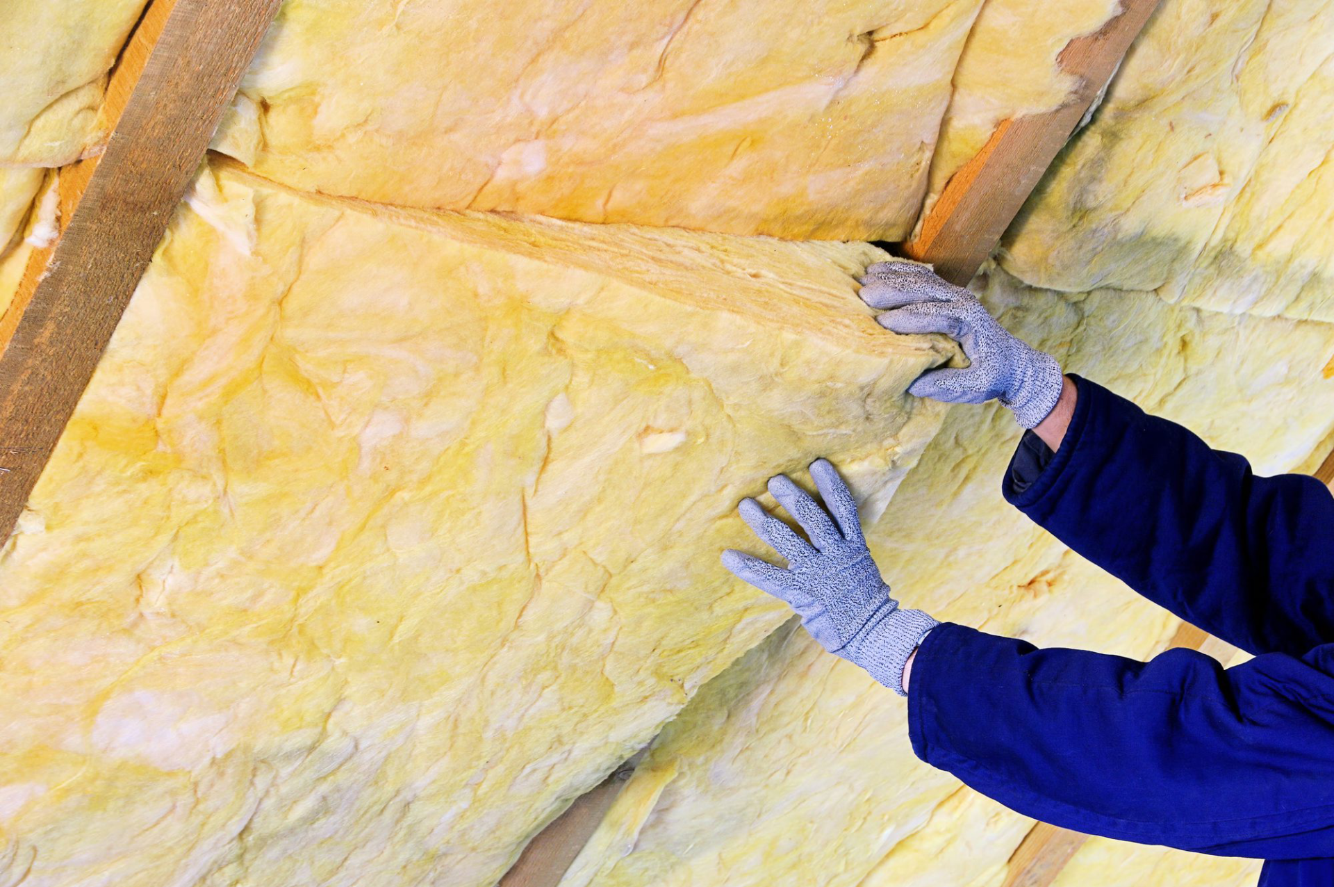 Person installing fiberglass insulation in attic