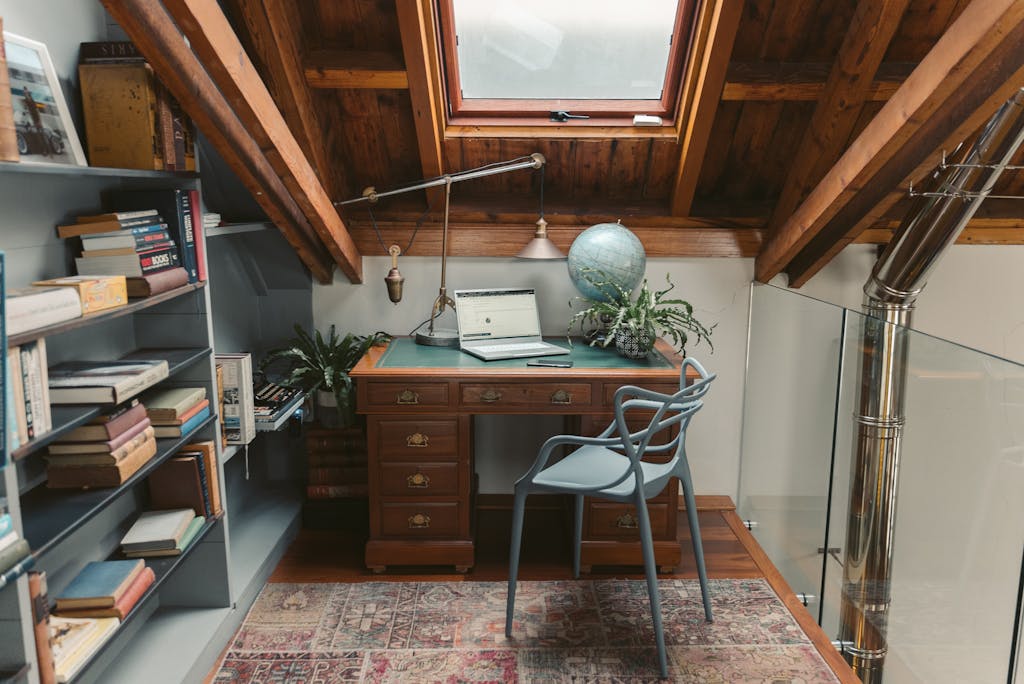 A cozy attic home office features a wooden desk, skylight, and ample books for an inspiring workspace.