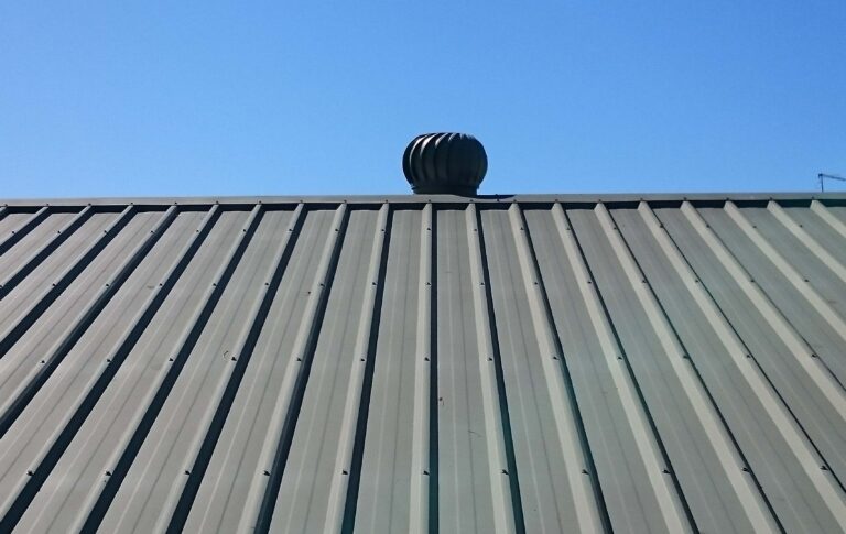 Metal roof with turbine vent under blue sky.