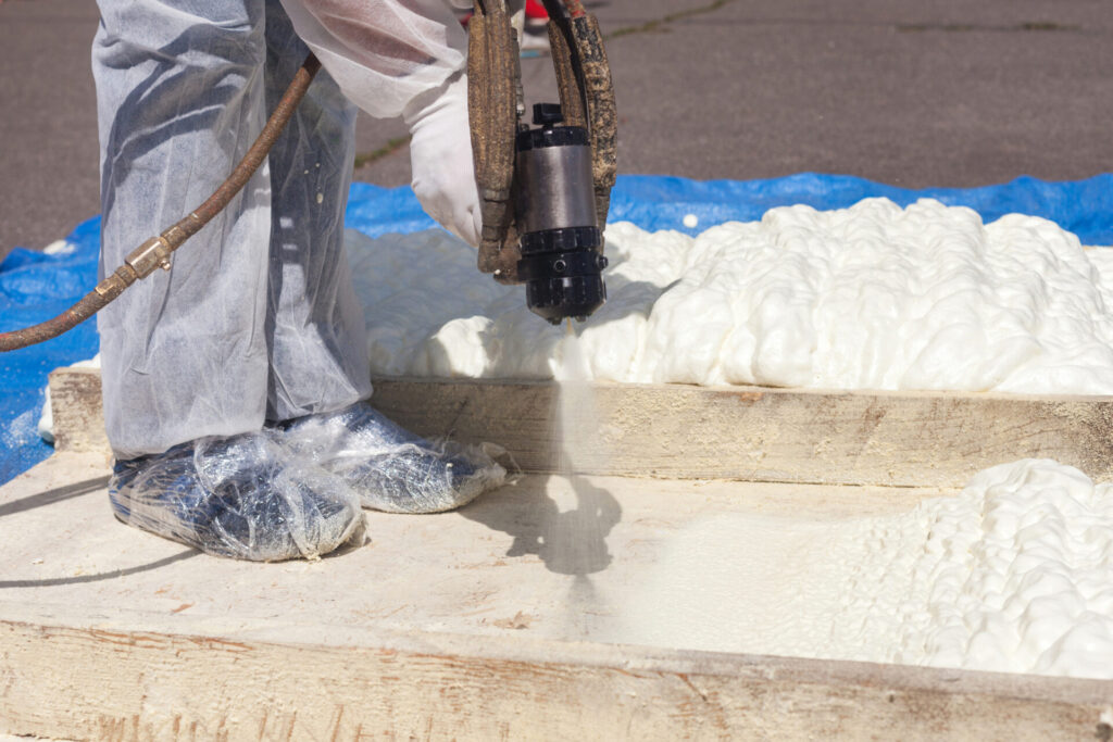 Technician dressed in a protective white uniform spraying foam insulation using Plural Component Spray Gun. Spraying polyurethane foam for roof and energy saving