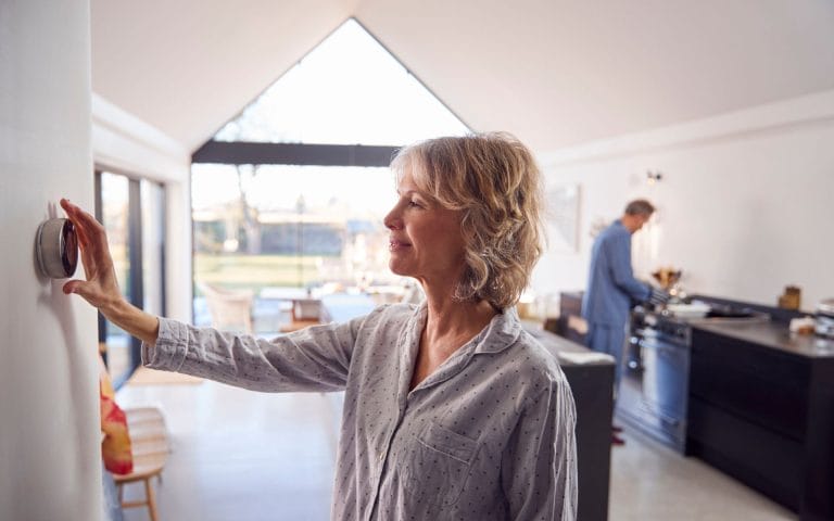 Women changes the thermostat on the wall. Temperature changes are a sign you are losing energy due to poor insulation.